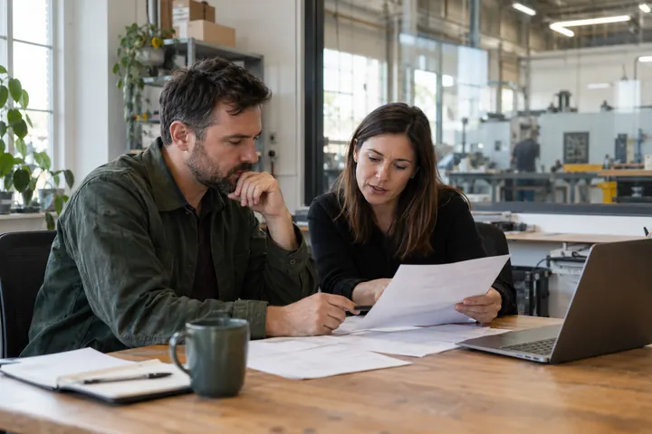 Business owner reviewing financing plans beside a manufacturing workshop